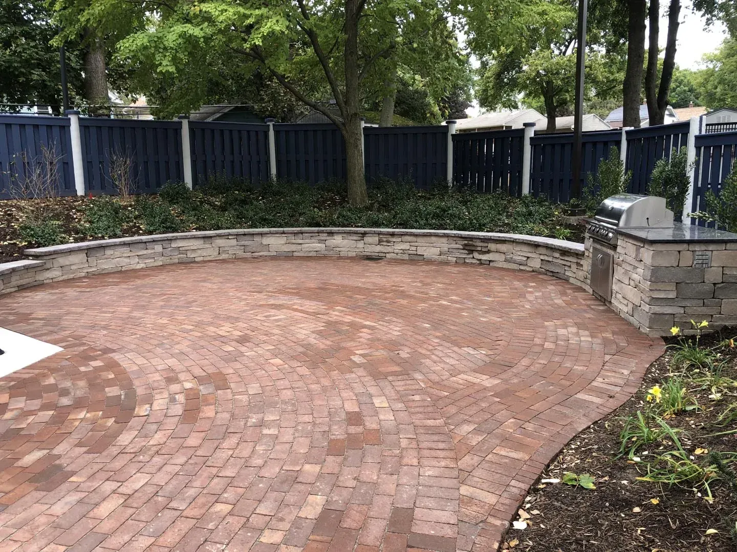 Circular red brick paver patio ringed by a stone seat wall with a built-in grill station