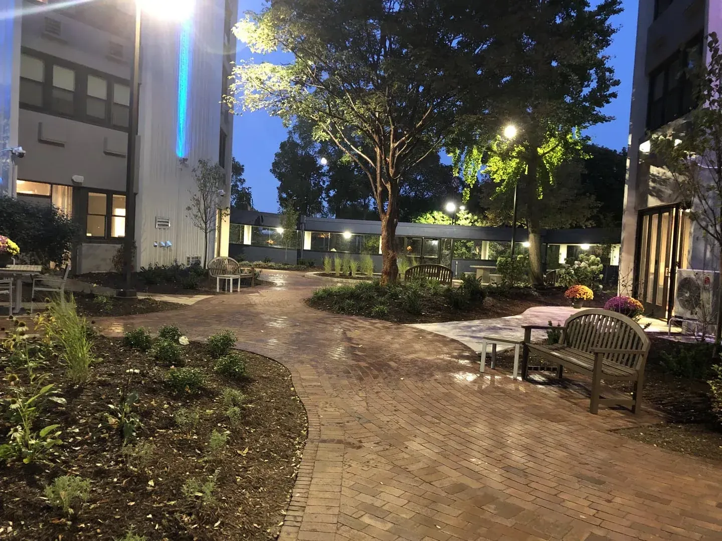 Lit commercial courtyard with paver walkways, seating, and planting beds in the evening