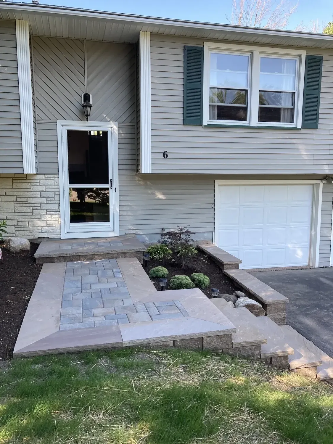 Rebuilt front entry with a paver landing, wide steps, a low retaining wall, and a fresh planting bed