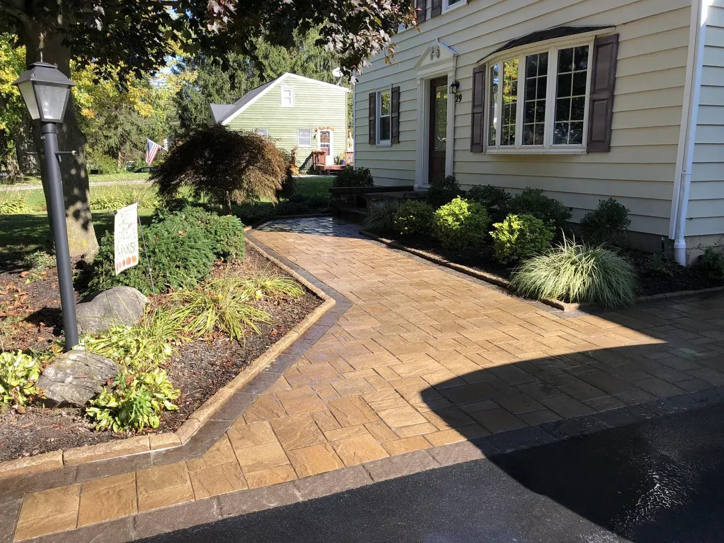 Wide curved paver walkway from driveway to front door beside newly planted foundation beds