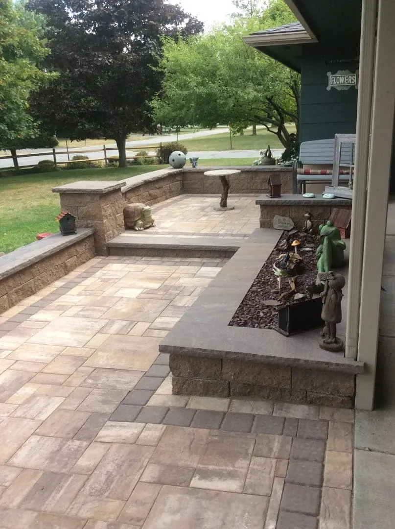 Multi-level paver patio with steps between levels and a stone seat wall enclosing the upper terrace