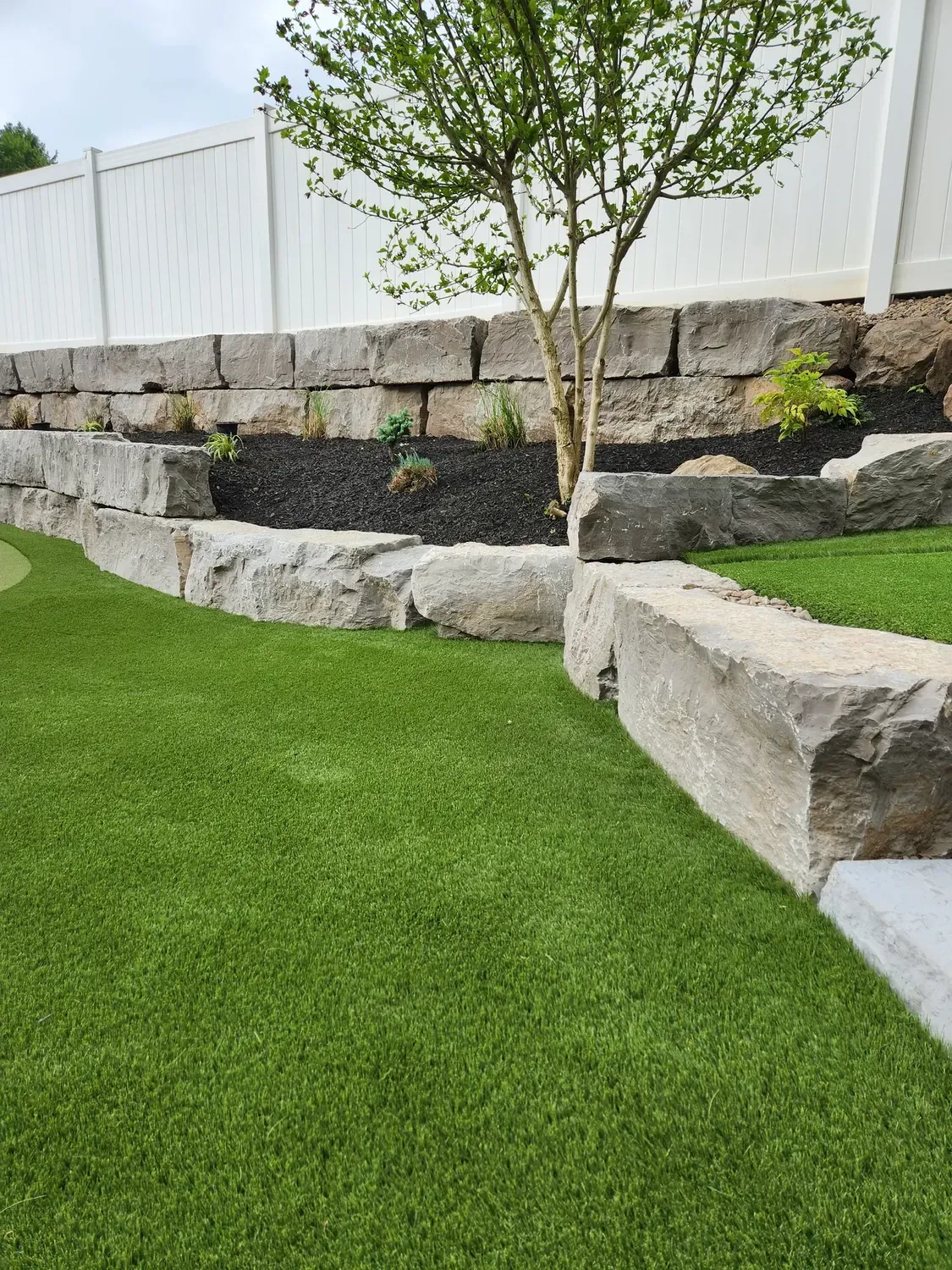 Contoured artificial putting green bordered by a natural stone wall and planted beds