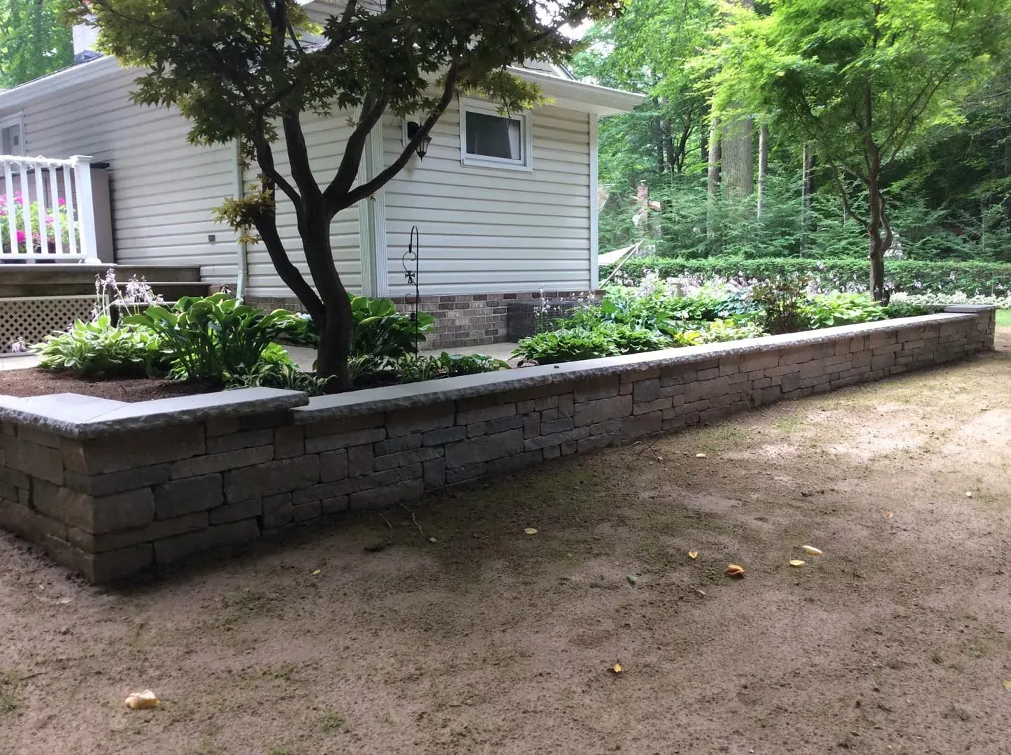 Long raised stone retaining wall creating a level planted shade garden beside a home