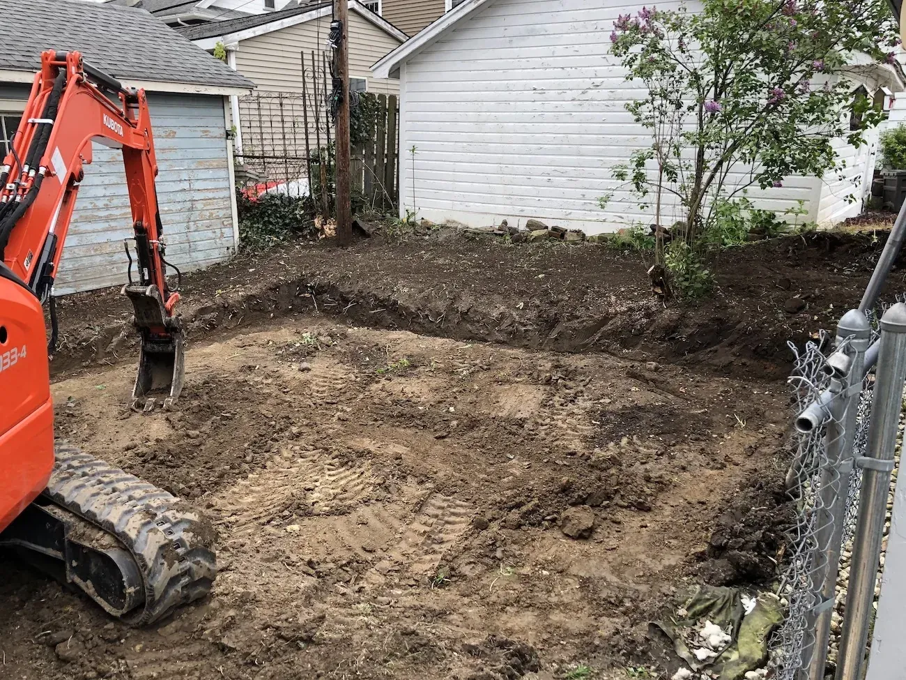 Compact excavator regrading a stripped-back side yard, with fresh machine tracks in the exposed soil